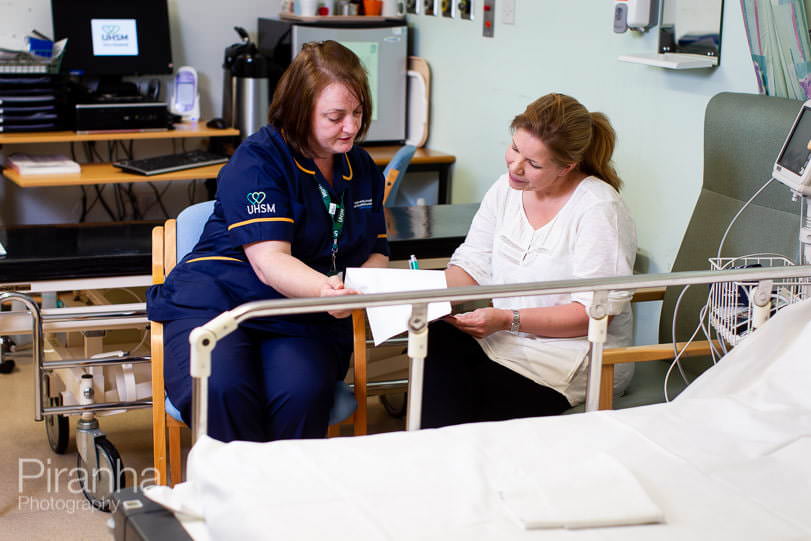 photograph of nurse explaining treatment to patient in hospital ward at Manchester hospital