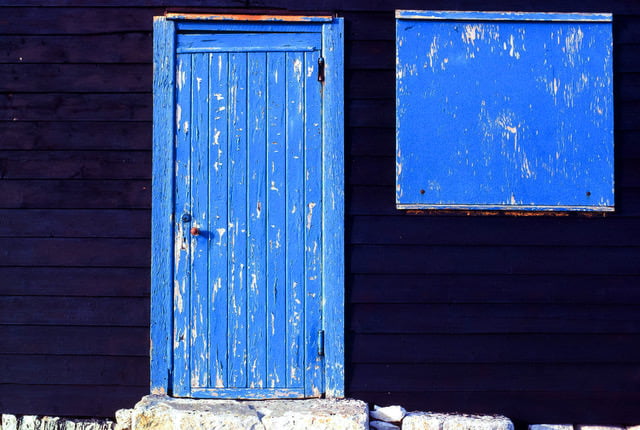 Close up photograph of blue wooden door and window of beah hut