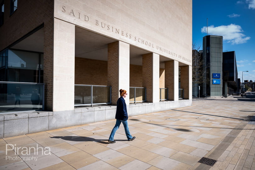 Teenage girl walking in front of an empty Said business school in Oxford with blue sky behind.