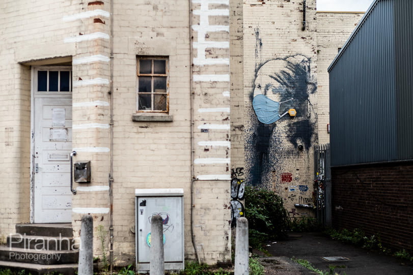 Photograph of Branksy Girl with the Pierced Eardrum graffiti with face mask